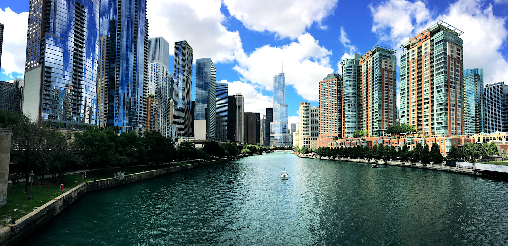 Downtown Chicago, Illinois. View over the river, with a boat seen floating down. Blue sky with clouds above, reflected in the glass of the buildings which line both sides.