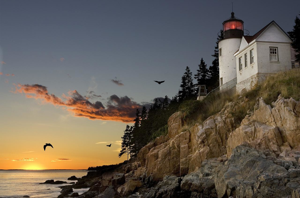 lighthouse in Maine is seen at sunrise, the sky a beautiful blue fading into yellow, pink, and orange as the lighthouse sits atop a cliff with the water below. Maine Officially Becomes 33rd State to Legalize Sports Betting