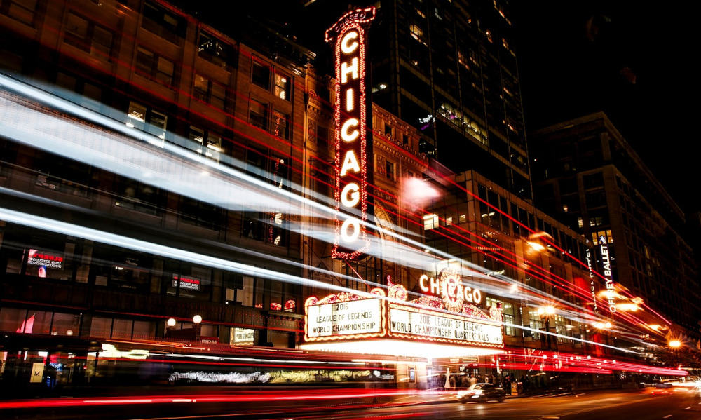The Chicago theater is seen at night, with neon lights and motion blur of car taillights as they drive down the street. Chicago is a big sports city & undoubtedly played a roll in Illinois impressive sports betting revenue numbers for its first full year.