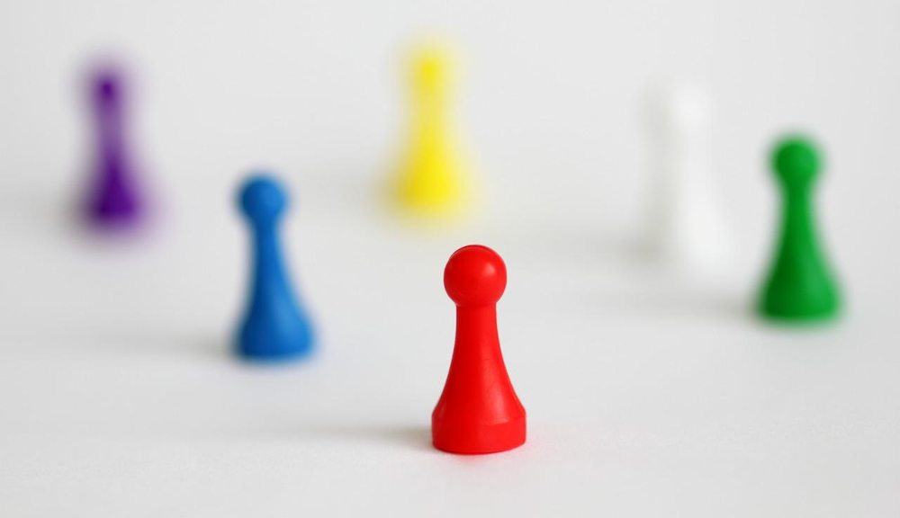 game pieces of various colors are seen, all but one are out of focus, but in the front is a red pawn that is standing out from the crowd and in focus