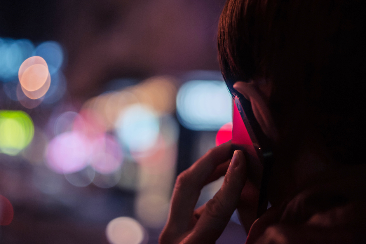 a young person is seen talking on their mobile phone in NYC at night. Rising Concerns: NY Gambling Helpline Calls Surge 26%